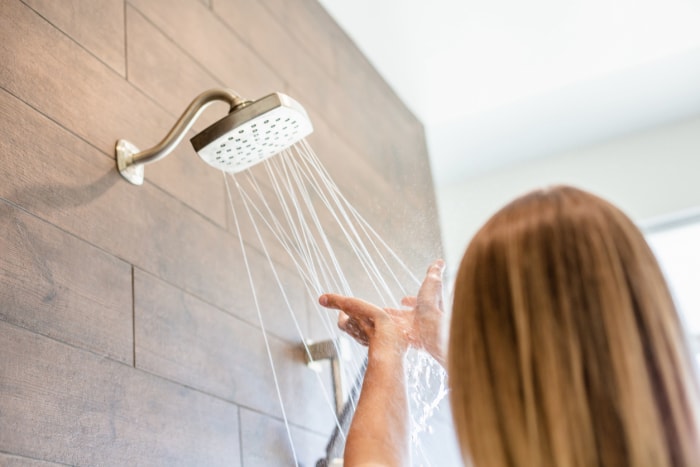 Une femme passe ses mains sous l'eau qui coule de la pomme de douche dans la salle de bains.