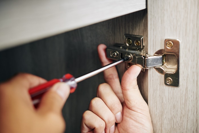 Gros plan d'un bricoleur assemblant une armoire de cuisine et vissant une charnière de porte