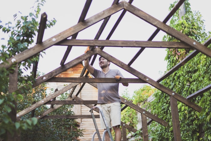 Un homme en short kaki construit une pergola dans une arrière-cour verdoyante.