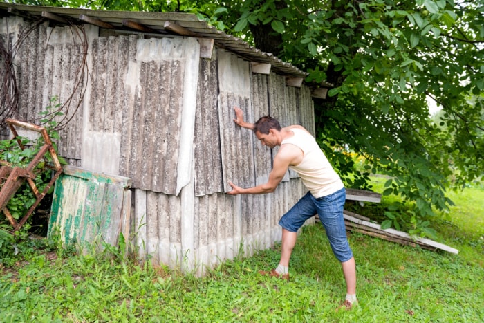 Homme essayant de démolir un vieux hangar.