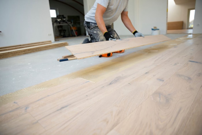 Homme d'âge moyen aux cheveux gris posant un parquet en bois d'ingénierie, démontrant la belle esthétique et la durabilité du matériau.