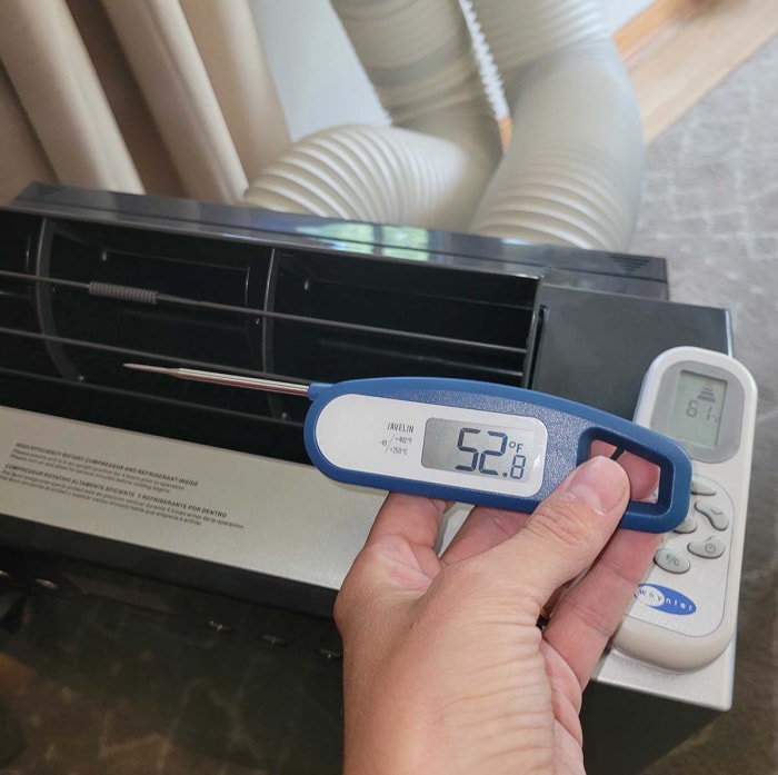 Une personne tenant un thermomètre numérique à côté d'un climatiseur portable Whynter