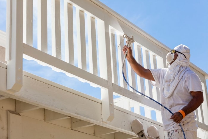 Un professionnel utilise un pulvérisateur de peinture pour appliquer de la peinture blanche sur une terrasse en bois.