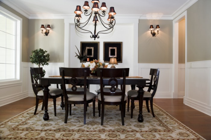 a-traditional-style-black-dinign-table-and-chairs-under-a-black-chendelier-and-in-a-beige-room-withwhite-wainscotting