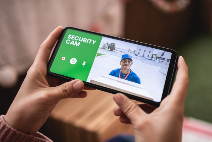 iStock-1349268379 homme sonnant à la porte avec une caméra sur son téléphone