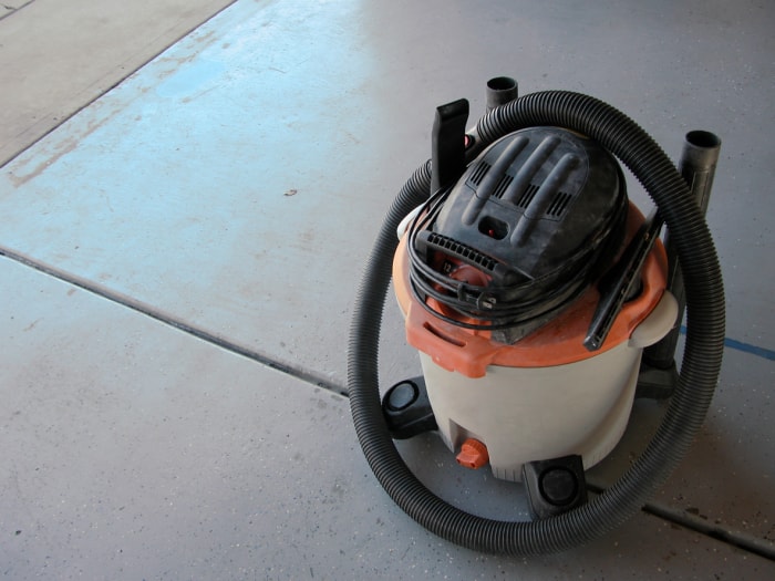 Un aspirateur d'atelier posé sur le sol du garage entre deux nettoyages.