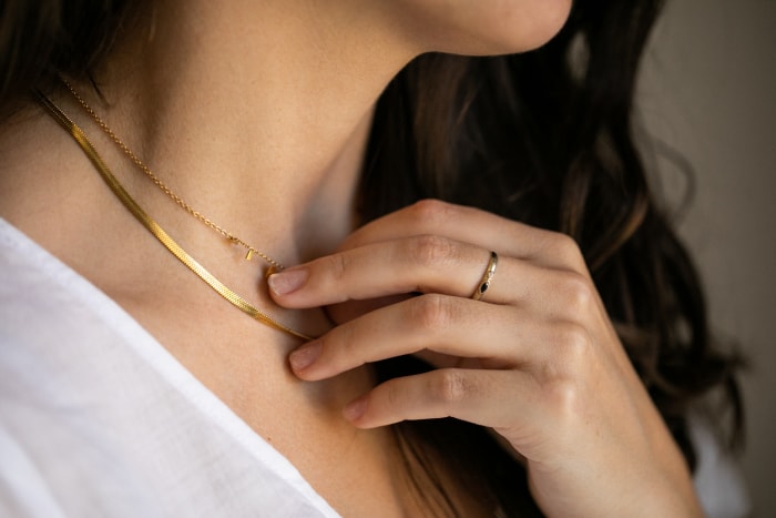 gros plan sur le cou d'une femme brune en t-shirt blanc portant un collier en or et une bague sur une main