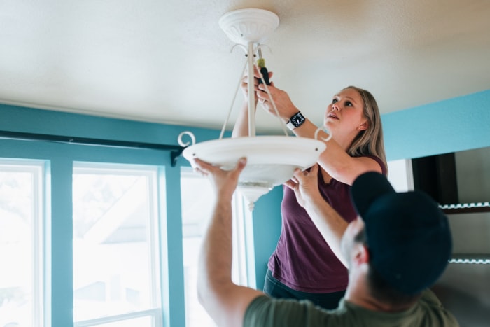 Un jeune couple change l'ampoule d'un luminaire au plafond.