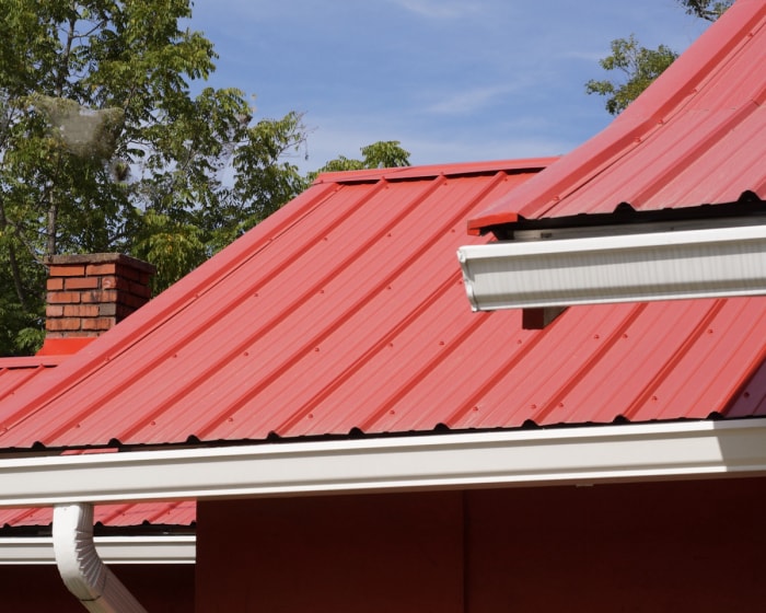 Une maison avec une cheminée en brique et un toit en métal rouge.