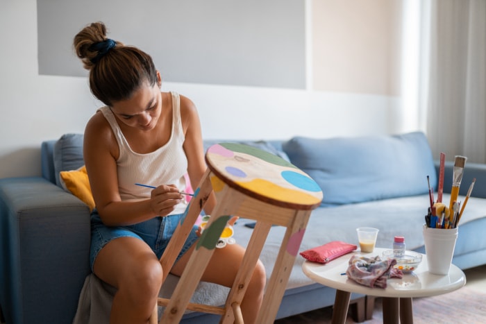 jeune femme dans le salon peignant un tabouret en bois avec plusieurs couleurs