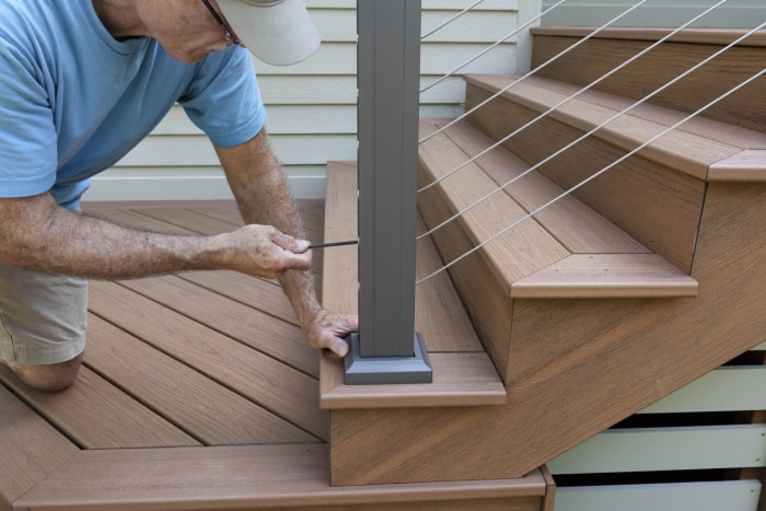 Un ouvrier utilise une clé Allen pour serrer la balustrade en fil de fer sur une nouvelle terrasse en bois composite avec des marches.