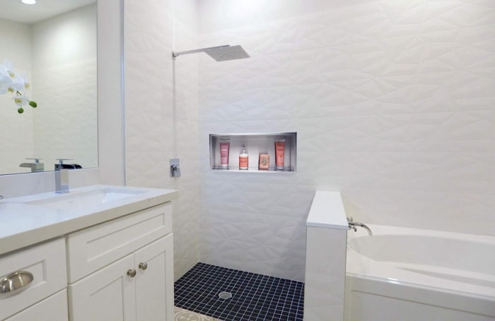 salle de bain blanche avec tube et lavabo blancs avec niche de douche en acier inoxydable au milieu du mur