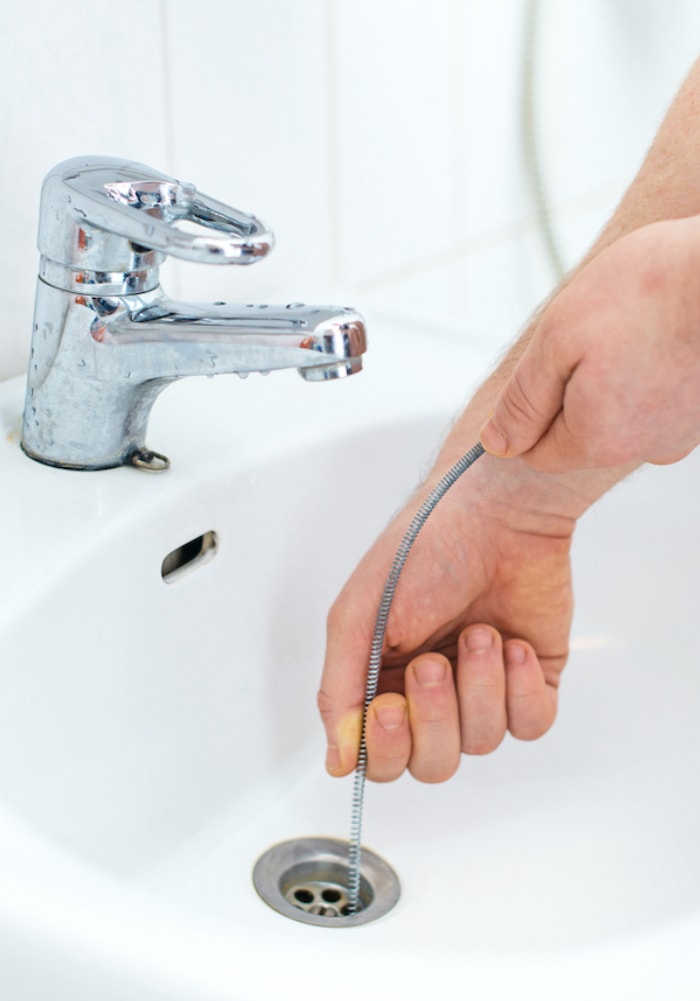 personne utilisant un serpent de vidange pour déboucher un évier de salle de bain