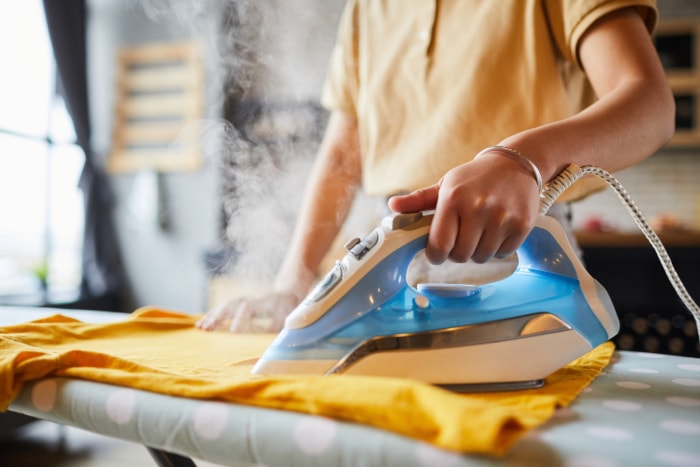 femme repassant une chemise jaune sur une planche à repasser