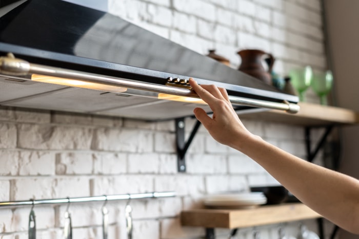 la main d'une femme appuie sur le bouton de la hotte noire de la cuisine pour l'allumer