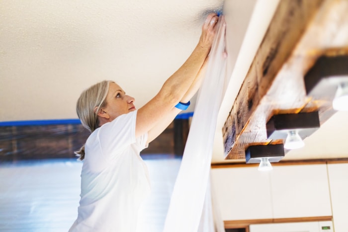 Femme adulte utilisant du ruban de peintre et du plastique pour la préparation de la peinture ; rénovation d'une résidence privée.