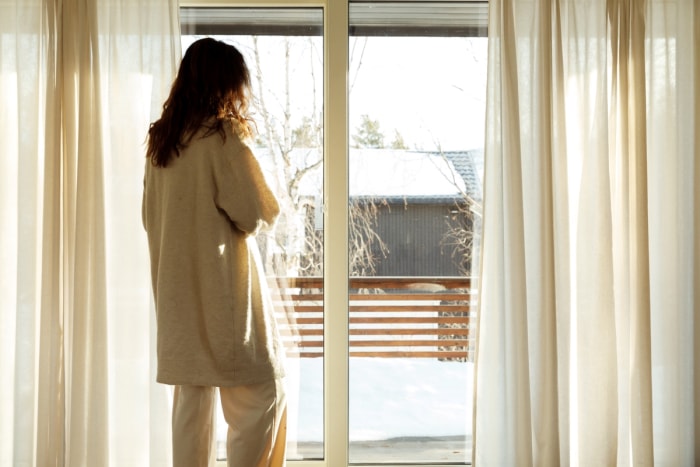 Femme debout à côté de rideaux ouverts.