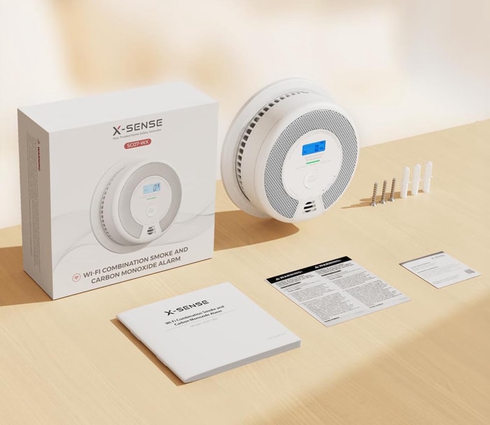 Gros plan d'un détecteur de fumée X-sense et de ses composants et de son boîtier disposés sur une table. 