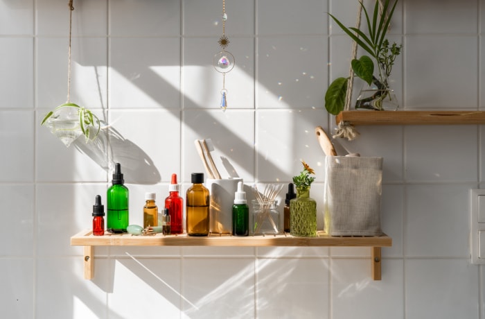 divers produits de beauté sur une étagère en bois sur un mur carrelé blanc dans la salle de bain