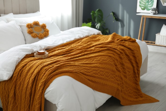 Lit confortable avec des draps blancs moelleux et un tricot orange.