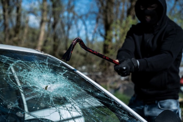 Un cambrioleur brise la vitre d'une voiture.