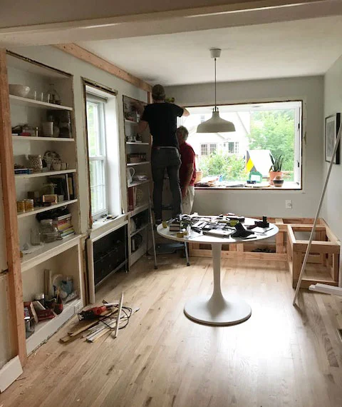 Deux personnes travaillent à la rénovation d'un coin déjeuner avec étagères intégrées et table tulipe.