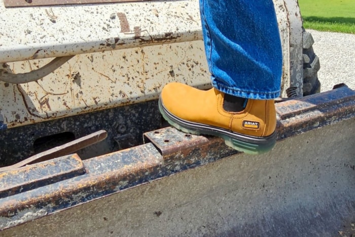 Personne portant des bottes de travail Ariat marchant sur l'arrière d'un skid steer