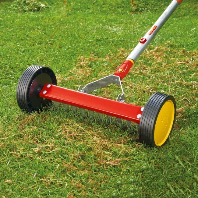 Un râteau à rouleaux manuel rouge sur de l'herbe verte.