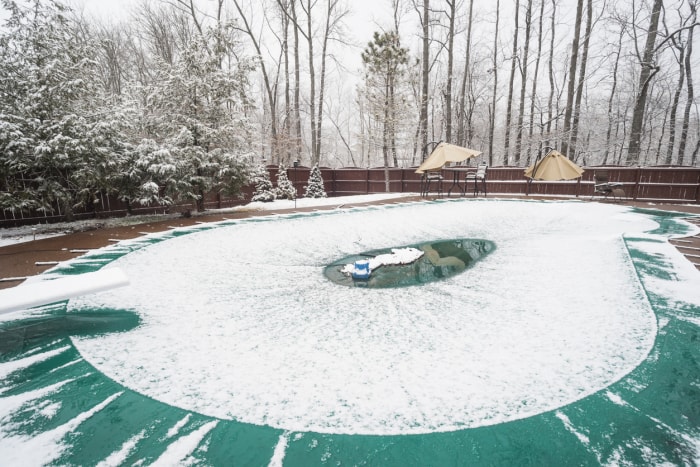 La neige fond au centre d'une couverture de piscine entourée d'arbres d'hiver