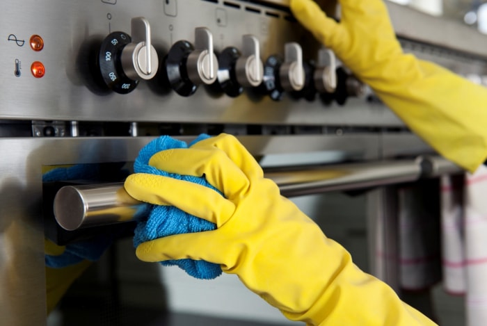 Mains gantées de jaune nettoyant une cuisinière en acier.