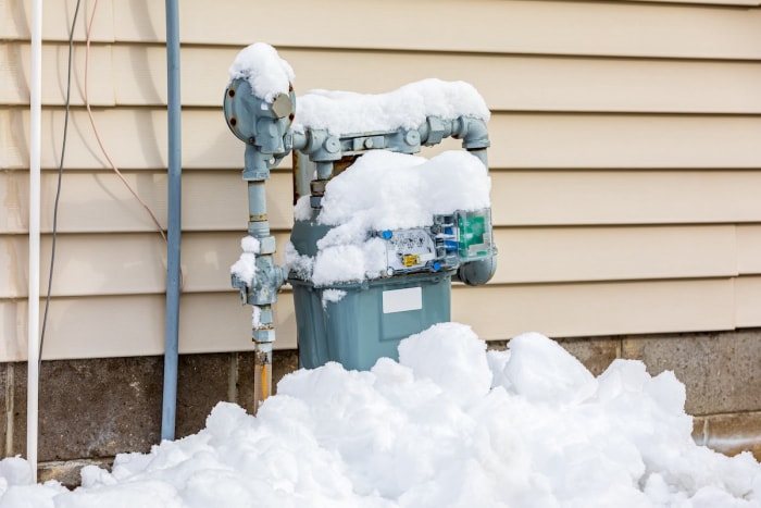 Un compteur de gaz résidentiel à l'extérieur d'une maison recouverte de neige pendant l'hiver, lorsque les factures de gaz peuvent augmenter en raison de la consommation.