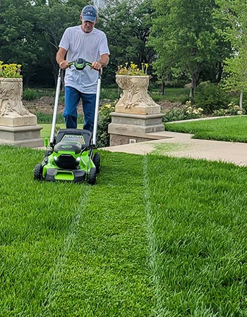 Une personne utilisant la tondeuse à batterie Greenworks Pro 60V 21 pouces pour tondre une pelouse d'un vert éclatant.