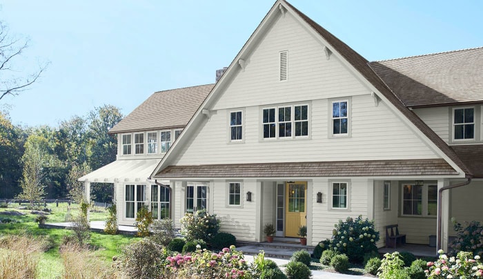 Une maison à deux étages est peinte dans un blanc cassé crémeux et entourée d'un aménagement paysager verdoyant.