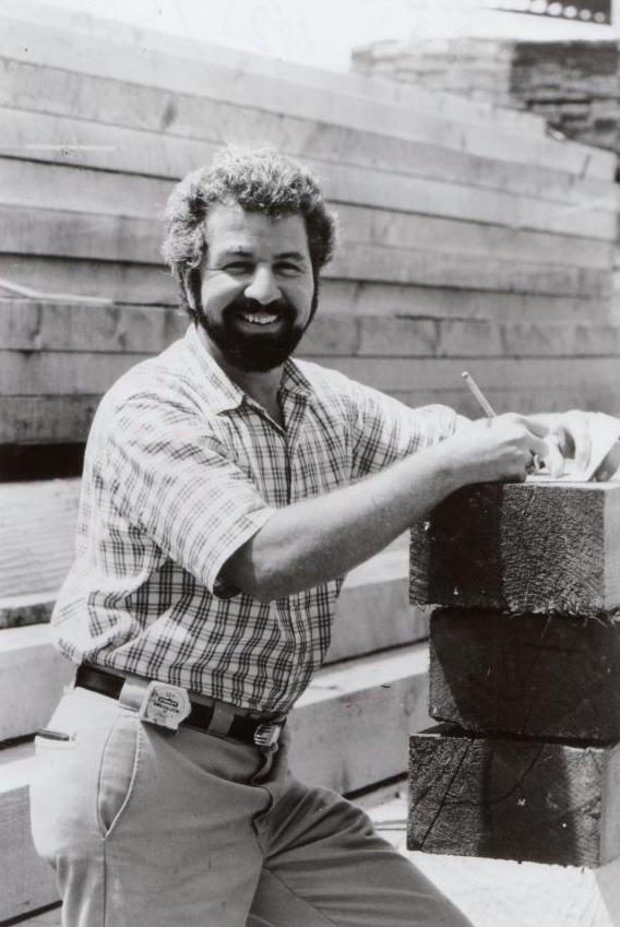 Bob Vila, en chemise à carreaux, cheveux et barbe, écrit quelque chose sur le chantier.