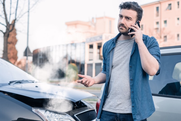 un homme passe un appel tandis que de la fumée sort du capot d'une voiture.