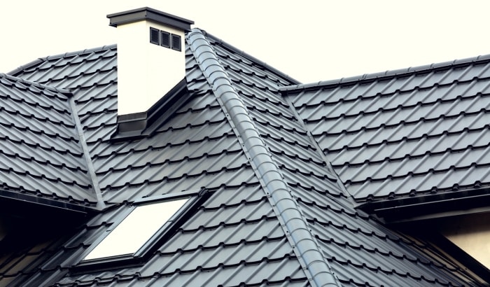 Toiture d'une maison neuve avec pentes, lucarne, cheminée enduite et grilles de ventilation. Couverture du toit avec tuiles en acier.