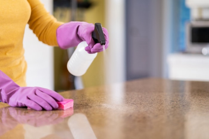 Une personne pulvérisant un comptoir de cuisine avec un flacon pulvérisateur.