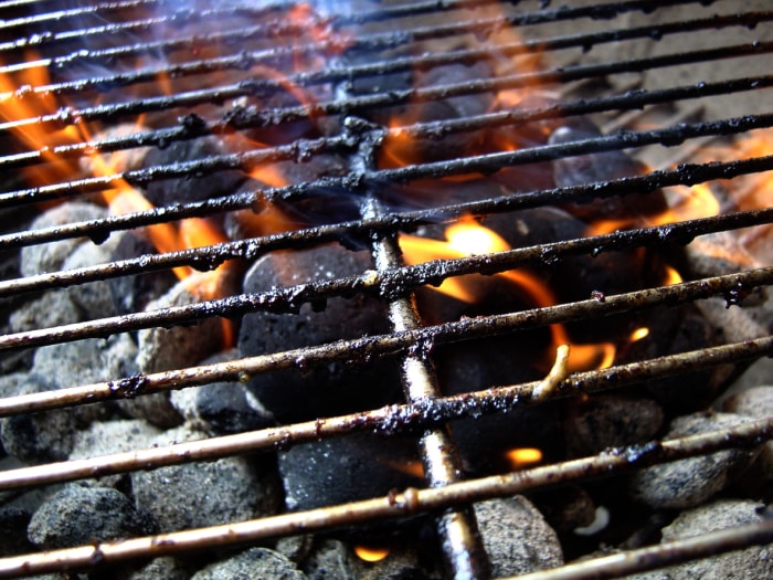 gros plan sur un gril recouvert de graisse carbonisée avec des flammes et du charbon de bois en dessous