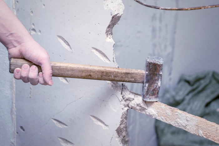 Personne tenant une masse sur un mur défoncé.