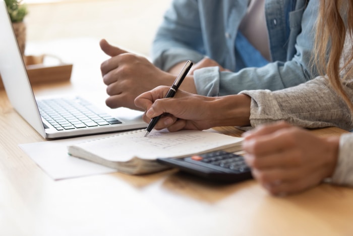 Un couple calcule un budget avec un ordinateur portable, un cahier et une calculatrice.