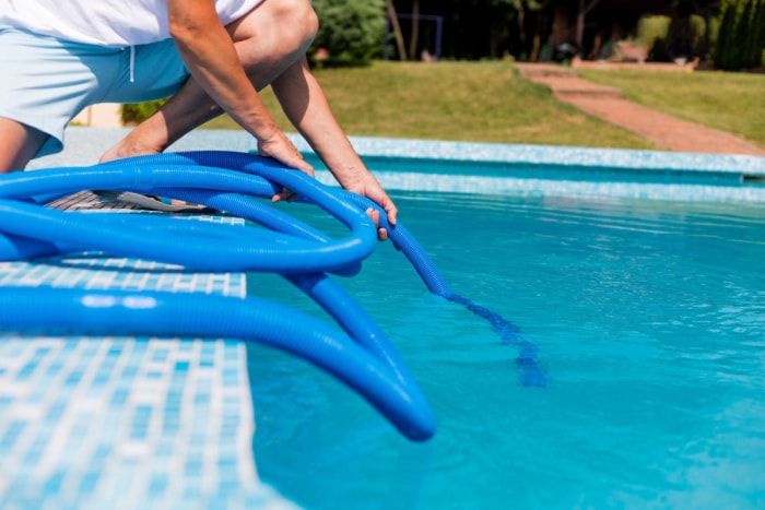 Gros plan d'une personne nettoyant une piscine avec un tuyau bleu. 