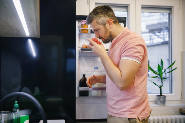 Homme sentant des tomates dans le réfrigérateur