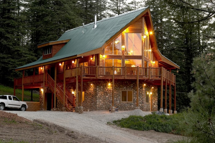 Une cabane en rondins illuminée de lumières le soir avec un toit en métal vert.