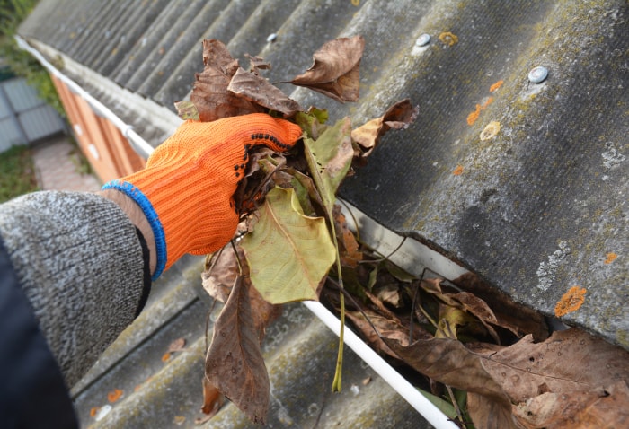 Une personne portant des gants de travail orange nettoie les feuilles des gouttières