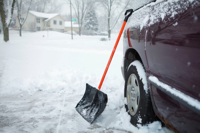 Pelle à neige appuyée sur la voiture.