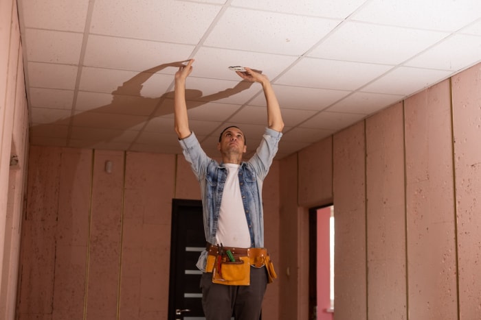 Un réparateur pousse sur des dalles de plafond suspendu.