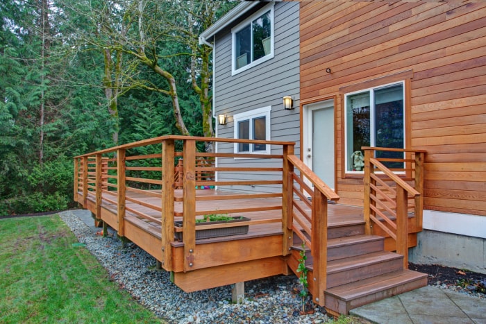 Charmante maison récemment rénovée, avec son extérieur en bois naturel et son revêtement gris qui lui confèrent un bel attrait extérieur. Vue détaillée d'une jolie terrasse avec rampes en bois.