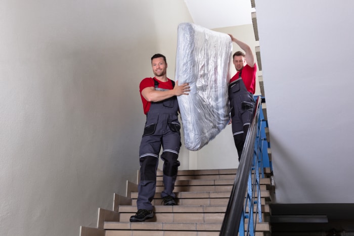 Deux jeunes déménageurs en uniforme transportant le matelas emballé tout en descendant l'escalier