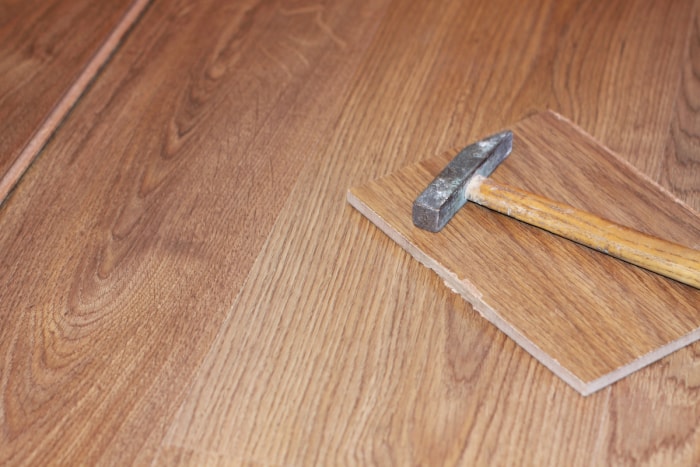 Un marteau et une planche de parquet imitation bois cassée reposent sur un autre revêtement de sol stratifié.