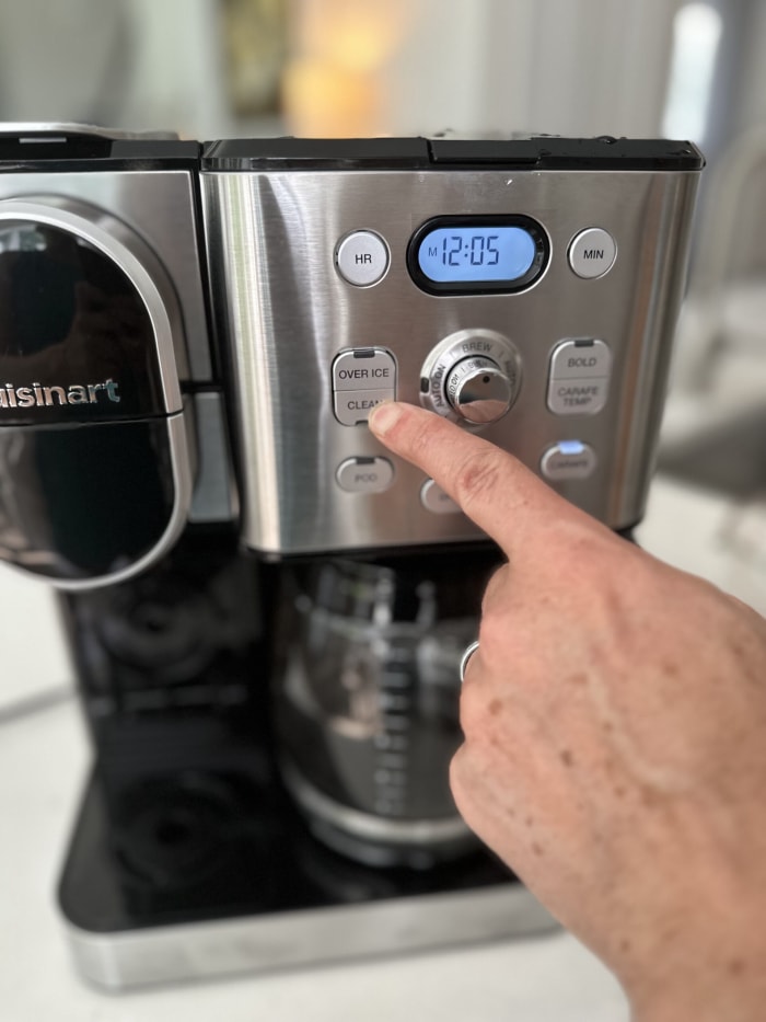 gros plan d'une cafetière avec la main d'un homme appuyant sur le bouton de nettoyage